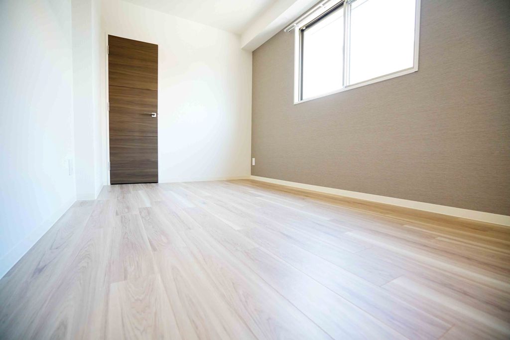 Gate Court Higashimikuniの東面窓付き6.5帖洋室:フローリングは木目調のベージュ、クロスはグレイ、建具はダークブラウン